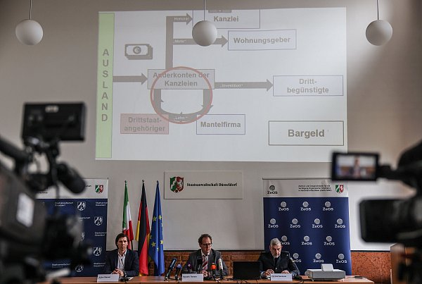 Hendrik Timmer (Mitte), Staatsanwalt in Düsseldorf, berichtet am Mittwoch mit einem Schaubild über die Ergebnisse der Razzia gegen eine Schleuserbande. - © Oliver Berg/dpa