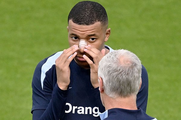 Kylian Mbappé trägt ein Pflaster auf der lädierten Nase und spricht in der Paderborner Home-Deluxe-Arena mit Trainer Didier Deschamps. - © AFP or licensors