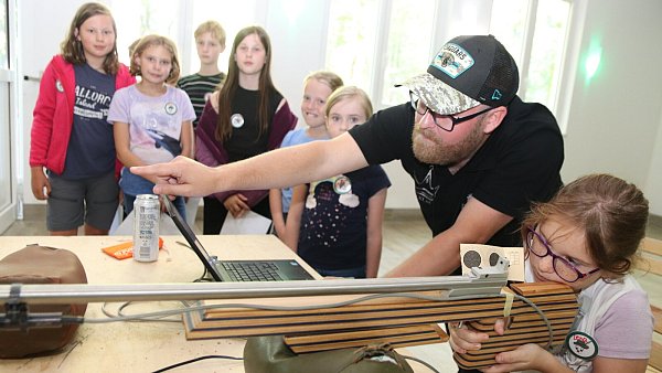 Niklas Kramer zeigt Lena, wie sie beim Schießen mit dem elektronischen Scatt-Gewehr das mehrere Meter entfernte Ziel anvisieren kann. - © Knut Dinter