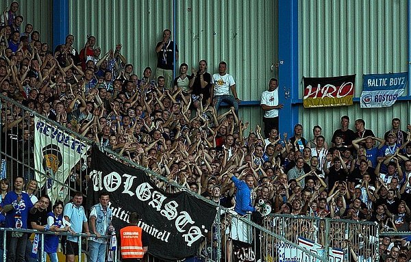 Die Banner der Rostock-Fans sprechen Bände. Ein Wachschützer in oranger Weste steht vor der Flagge der berüchtigten "Wolgastä", die sich selbst als "multikriminell" bezeichnen. - © FOTO: OLIVER KRATO