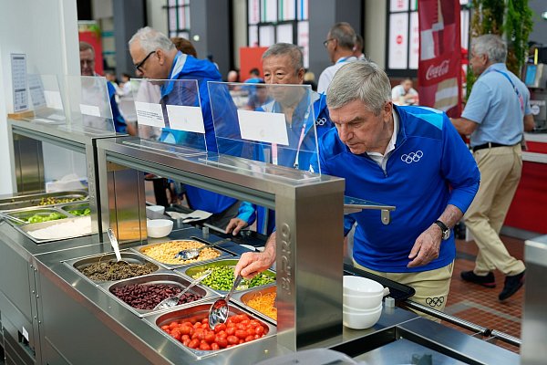 IOC-Präsident Thomas Bach langt in der Mensa des olympischen Dorfs zu - © David Goldman/AP Pool/dpa