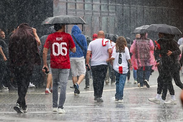 Das haben sie sich sicherlich anders vorgestellt: Fussballfans in Dortmund laufen im strömenden Regen zum Stadion. - © Christoph Reichwein/dpa