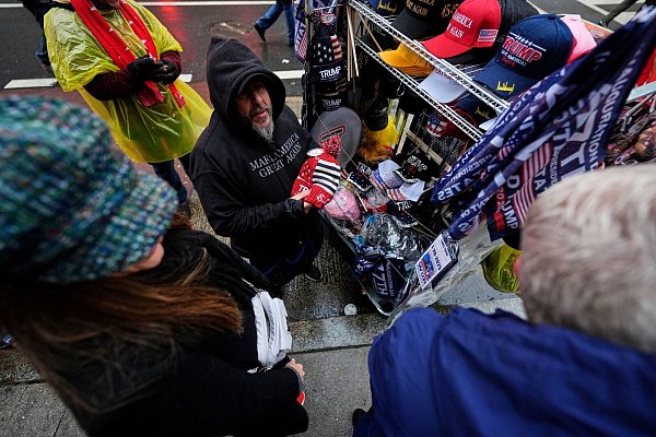 Dieser Straßenverkäufer wird vor der Arena, in der Trump später spricht, einiges an Merchandise-Artikeln los. - © Mike Stewart/AP/dpa