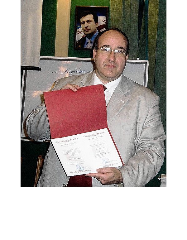 Vor dem Bild des georgischen Staatspräsidenten Micheil Saakaschwilli zeigt Christoph Werth stolz seine Urkunde der Ehrendoktorwürde der Universität Kutaissi. - © FOTO: PRIVAT