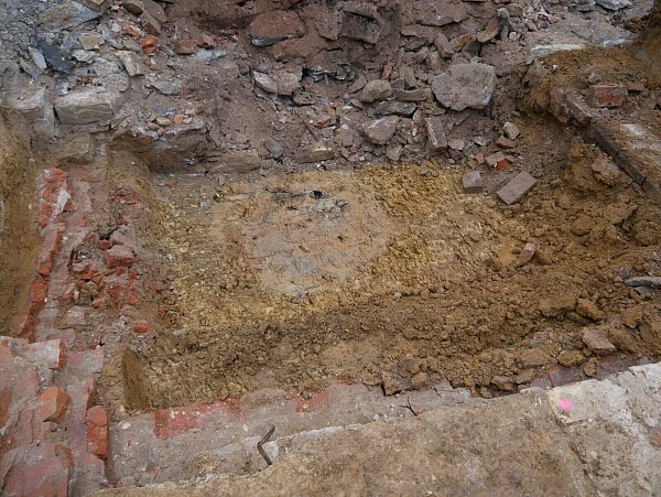 Blick auf die Fundamente des Lazaretts. Zwischen ihnen zeichnet sich die hellgraue Verfüllung des runden Brunnenschachtes (Bildmitte) im gelben Lehmboden ab. - © EggensteinExca/Süße