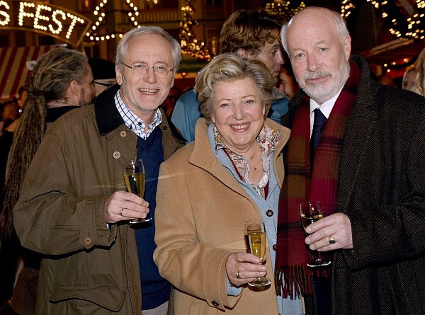 Die Schauspieler Joachim Hermann Luger (Hans Beimer, links) und die Schauspieler Marie-Luise Marjan (Mutter Beimer) und Bill Mockridge (Erich Schiller, rechts) posieren in der Außenkulisse mit Sektgläsern nach der Live-Ausstrahlung der 1559. Folge im Dezember 2015. - © picture alliance / dpa