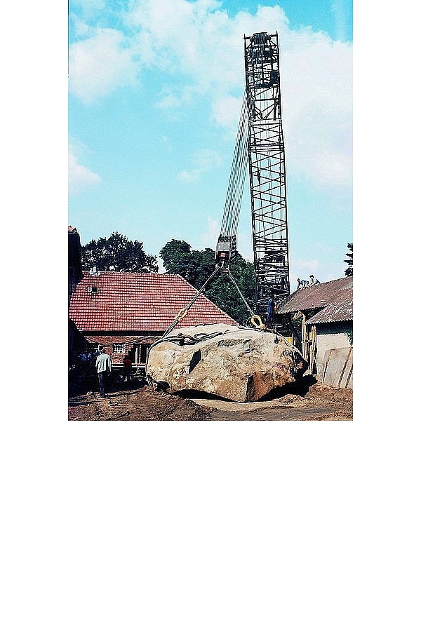 Der steinerne Gigant liegt auf dem Erdboden. Rechts auf der Scheune entfernen Helfer einen Teil des Dachstuhls, um Platz für den Autokran zu schaffen. - © ARCHIVFOTOS: W. HORSTMANN