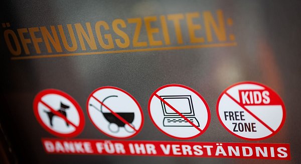 An einer Scheibe der Café-Bar 8tto Grammi weist ein Schild auf das Verbot von Laptops hin - wie auch auf das Verbot für Hunde, Kinderwägen und auf eine kinderfreie Zone. - © Daniel Karmann/dpa