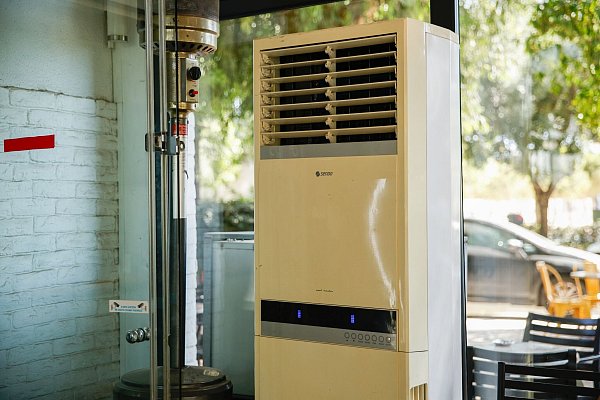 Athen: Eine mobile Klimaanlage steht im verglasten Innenraum eines Cafés. (Archivbild) - © Socrates Baltagiannis/dpa