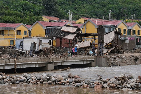 Dorfbewohner versammeln sich in der Nähe einer Brücke, die nach schweren Regenfällen im Bezirk Miyun am Stadtrand von Peking überflutet wurde. - © Andy Wong/AP/dpa