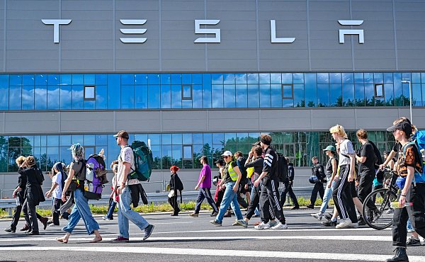 Teilnehmerinnen und Teilnehmer eines Protestmarschs laufen am Tesla-Werk vorbei. - © Patrick Pleul/dpa