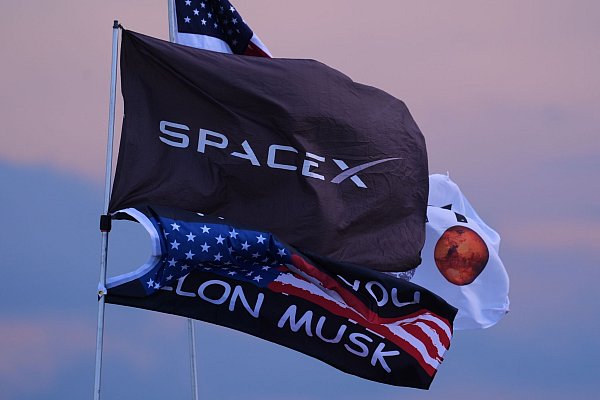 Mehrere Fahnen, darunter zwei mit dem Aufdruck SpaceX und Elon Musk, sind in der Nähe des Startortes. - © Eric Gay/AP/dpa