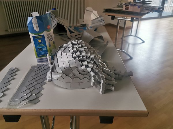 Ein kunstvoller Helm, der aus alten Milchtüten gebastelt wurde, liegt auf einem Tisch. - © Ramona Wahner/Deutsche Fastnachtakademie/dpa