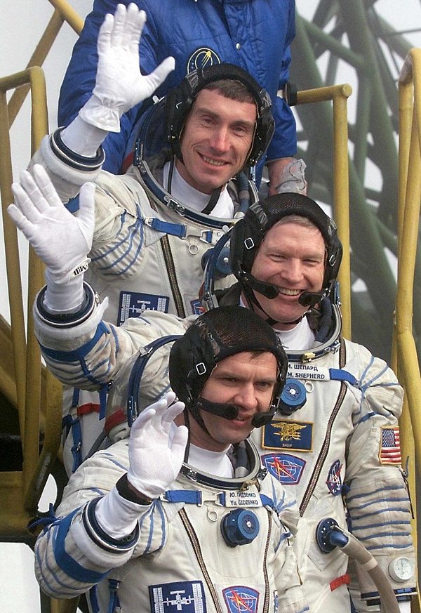 Der Kommandant der ersten Langzeitmission zur Internationalen Raumstation, der amerikanische Astronaut Bill Shepherd (M), und die russischen Kosmonauten Juri Gidsenko (unten) und Sergej Krikaljow (oben) winken, bevor sie auf dem Kosmodrom in das Raumschiff "Sojus-TM-31" einsteigen. (Archivbild) - © Sergei Chirikov/epa/dpa