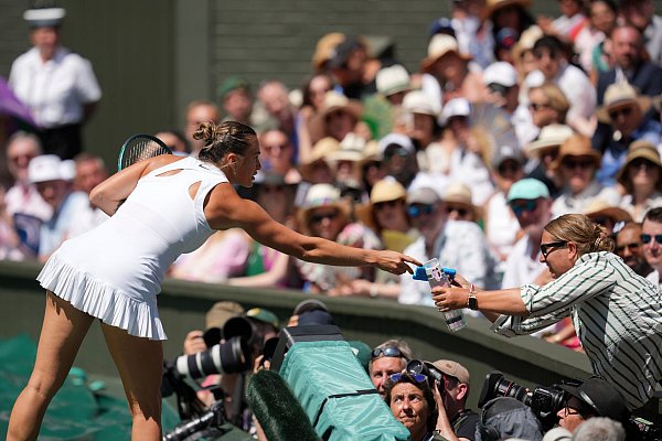 Aryna Sabalenka bringt eine Wasserflasche und ein Kühlpack zur Tribüne, wo es einer Zuschauerin nicht gut geht. - © Kin Cheung/AP/dpa
