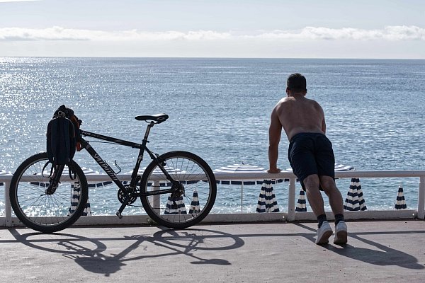Ein Mann mit nacktem Oberkörper macht am Strand von Nizza neben seinem Fahrrad Übungen. (Archivbild) - © Serge Haouzi/XinHua/dpa