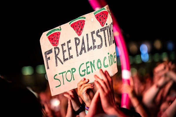 «Free Palestine - Stop Genocide» steht auf einem Plakat bei dem Auftritt vom US-Rapper Macklemore. Es war eine von wenigen politischen Botschaften im Publikum. - © Sina Schuldt/dpa