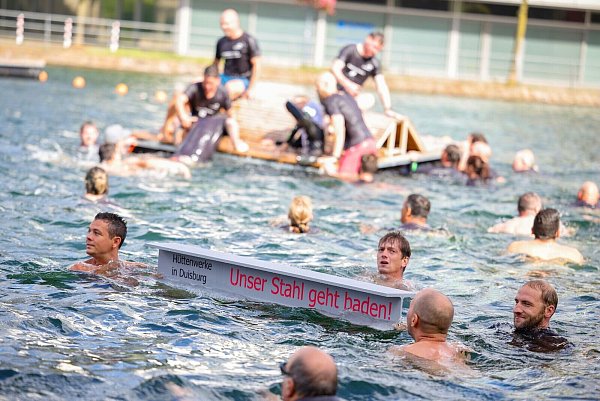 Ein symbolischer Stahlträger mit dem Slogan der Demo schwimmt im Duisburger Innenhafen zwischen zahlreichen Stahlbeschäftigten. - © Christoph Reichwein/dpa