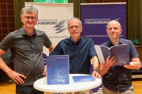 Friedrich Luchterhandt (Künstlerischer Betriebsdirektor, v. l.), NWD-Intendant Andreas Kuntze und Musikvermittler Johannes Hofmann stellen den NWD-Konzertkalender mit der großen "75" auf denm Cover vor. - © Ralf Bittner