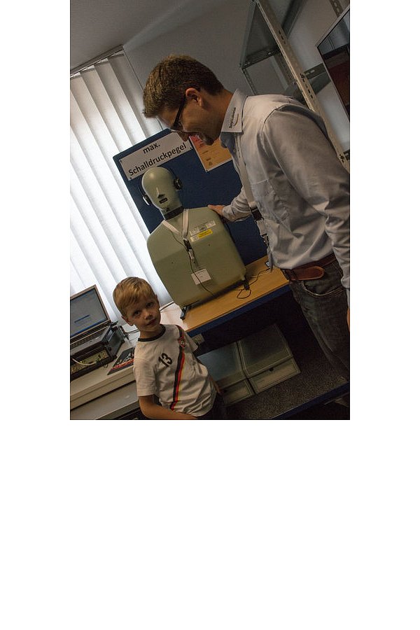 Der fünfjährige Lukas findet die "Mitarbeiterin Helga", wie es auf dem Namensschild des Dummys steht, interessant. Sie bekommt per Kopfhörer von Mitarbeiter Martin Schroeder kräftig was auf die Ohren. - © FOTO: ANJA SCHWEPPE
