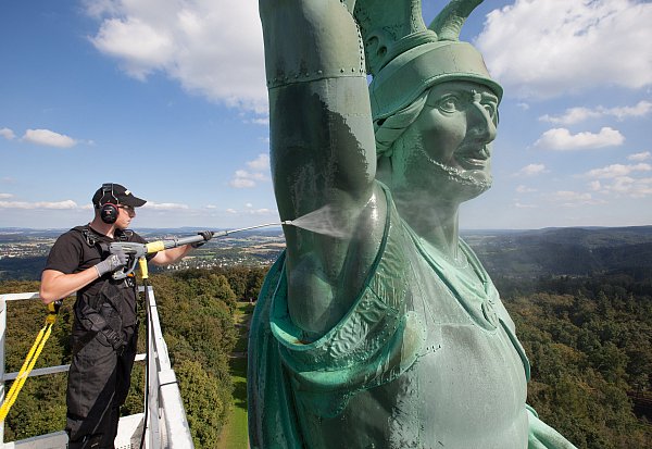 Der Mitarbeiter einer Reinigungsfirma spritzt das Hermannsdenkmal mit einem Reinigungsgerät ab. Dabei steht er auf einer mehr als 40 Meter hohen Hebebühne. - © dpa