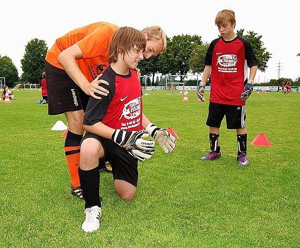 Lennart zeigt Felix wie er seinen Körper hinter den Ball bringt, Rico schaut aufmerksam zu.