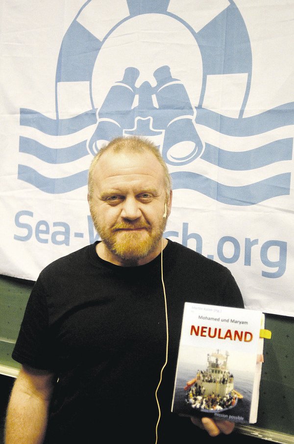 Hat Neuland betreten: Martin Kolek mit seinem Buch vor einem Banner des Rettungsschiffs Sea Watch. - © Dietmar Gröbing