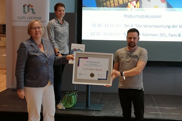 Gordon Knebel, Fanartikel-Produktmanager von Union Berlin, nahm die Auszeichnung aus den Händen von cum-ratione-Geschäftsführerin Kerstin Haarmann (l.) und Projektleiterin Lara Schröder entgegen. - © cum ratione