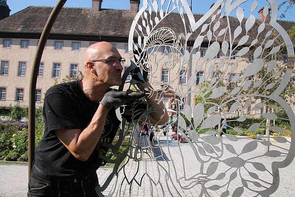 Künstler Hans Kordes mit Gartenschau-Botschafterin Holli im vergangenen Jahr im Corveyer Remtergarten. Auch die geflügelte Elfe aus Stahl wird ihren Platz am Wall finden. - © Huxarium