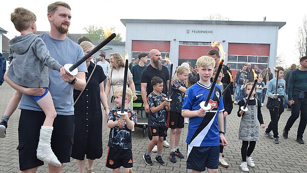 Lennard geht im Arminen-Trikot mit der Fackel voran. Viele weitere Kinder und Eltern folgen dem traditionellen Umzug zum Osterfeuer an die Lortzingstraße in Helpup. - © Karin Prignitz