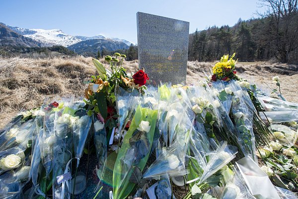 Inmitten von Blumen steht eine steinerne Gedenkstele mit der Aufschrift "In Erinnerung an die Opfer des Flugzeugunglücks vom 24. März 2015" in den vier Sprachen Englisch, Deutsch, Spanisch und Französisch. - © picture alliance / dpa