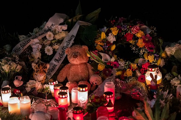 Ein Teddybär liegt neben Blumenkränzen und Kerzen auf dem Boden und erinnert an den tödlichen Messerangriff. - © Daniel Vogl/dpa