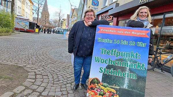 Das Schild zeigt’s an: Birgit Ischen (l.) und Sylvia Thiet von der Stadtverwaltung laden zu einem Bummel über den „kleinen, aber feinen Wochenmarkt“ ein. - © Madita Schellenberg