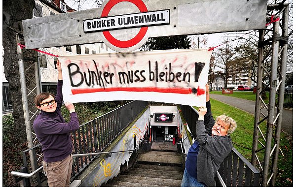Carsten Nolte, Leiter des Bunkers Ulmenwall, und Wolfgang Groß, Vorsitzender des Vereins Bunker Ulmenwall, befestigen über dem Eingang zum ehemaligen Luftschutzbunker ein Transparent, um für den Erhalt des Clubs zu demonstrieren. - © FOTO: ANDREAS FRÜCHT