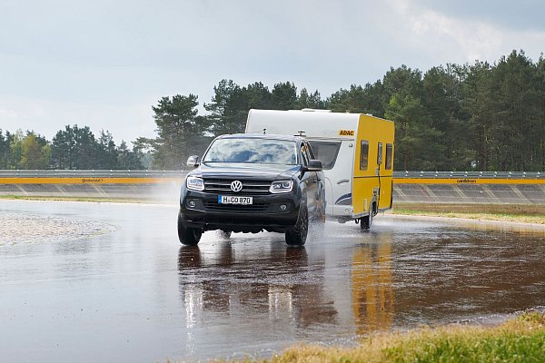 Ein Testwagen mit Anhänger demonstriert Fahrsicherheit auf regennasser Strecke. - © Marc Wittkowski/ADAC/dpa-tmn