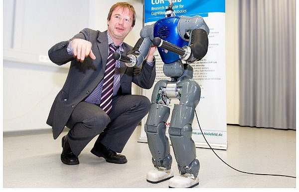 Professor Jochen Steil und Coman. Der humanoide Roboter hat noch keinen Kopf. Damit er nicht versehentlich umgestoßen und beschädigt wird, ist er nach oben hin gesichert. Coman hat schließlich mehr als 200.000 Euro gekostet. - © FOTO: CHRISTIAN WEISCHE