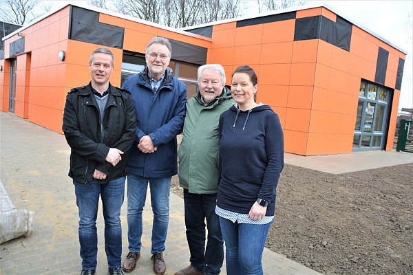 Architekt Christopher Davin, Verwaltungsleiter Uwe Wohlmann, Pfarrer Klaus Sommer und Kita-Leiterin Nina Michael (v. l.) stehen vor dem Anbau. Einige der orangefarbenen Platten für die Außenfassade fehlen noch. - © Karin Prignitz