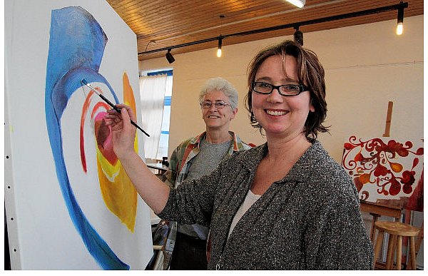 Kerstin Balzer hat sich für ein abstraktes Motiv entschieden. Anke Girod (hinten) schaut zu, wie sie die Ölfarbe auf die Leinwand aufträgt. Hinten rechts steht noch das Bild eines anderen Hobby-Künstlers auf der Staffelei. - © FOTOS: BOHNENKAMP-SCHMIDT